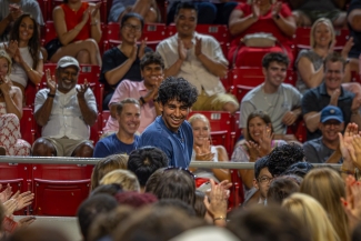 Student standing and smiling at the opening session. Onlookers also laughing and smiling supportively 