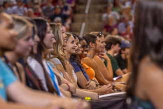 Students sitting in a row, smiling at the stage