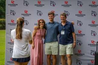 A family poses for a photo together in front of a Davidson College banner while someone takes their picture.