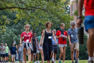A group of students and parents wearing orientation lanyards walk together along a tree-lined campus path during an event at Davidson College.
