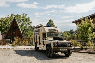 A vintage Land Rover ambulance custom-painted in cream and black sits parked in front of modern wooden cabins.