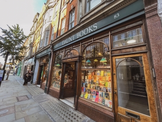 The exterior facade of Daunt Books featuring large arched glass windows filled with book displays along a city sidewalk.