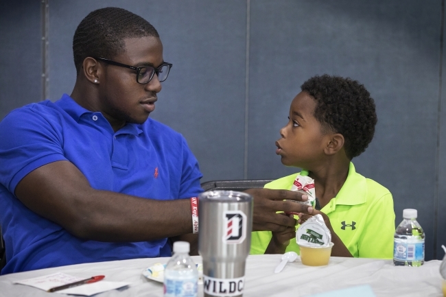 Student sits with young student and helps him open a juice carton