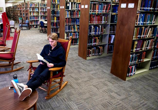 Student Reads Book in Library Rocking Chair