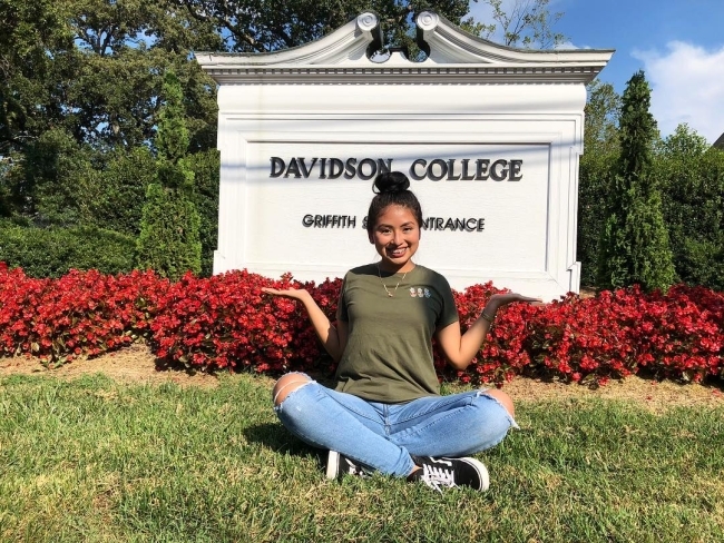 student sitting on the grass in front of the Davidson College sign