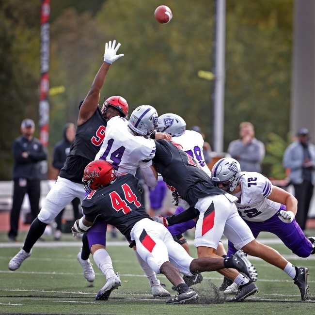 Pile Up of Football Players Reach for Ball Flying in the Air