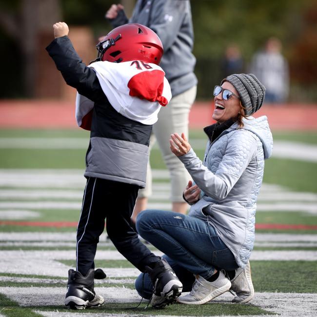 Little Boy in Davidson Football Uniform Cheers from Sidelines with Mom
