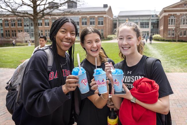 three Davidson students smile holding Pelicans snoballs and Davidson swag in Richardson Plaza