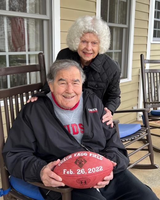 Dave seated in a rocking chair with a football in hand and Barbara Fagg next to him, smiling