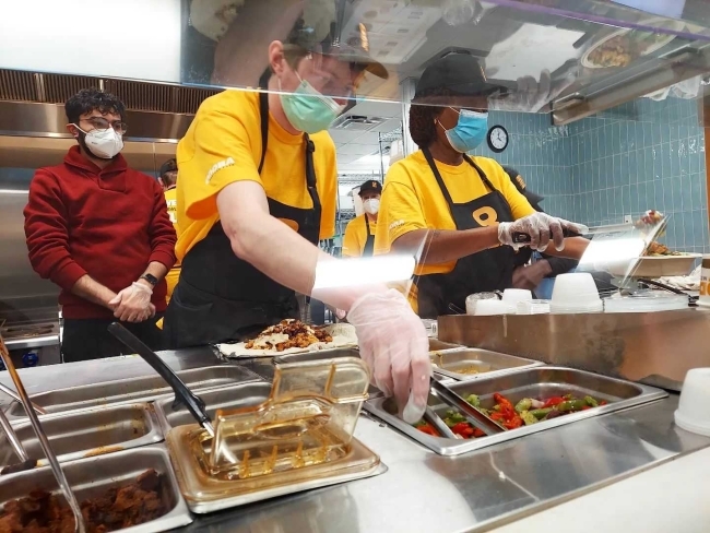 Qdoba staff grabbing peppers to place on a burrito