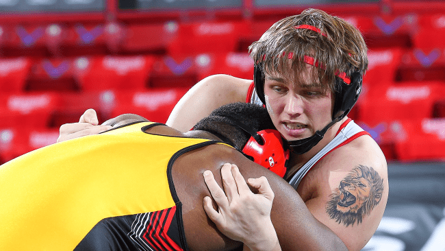 Jake Fernicola, a male student wrestling another student with red bleachers in background