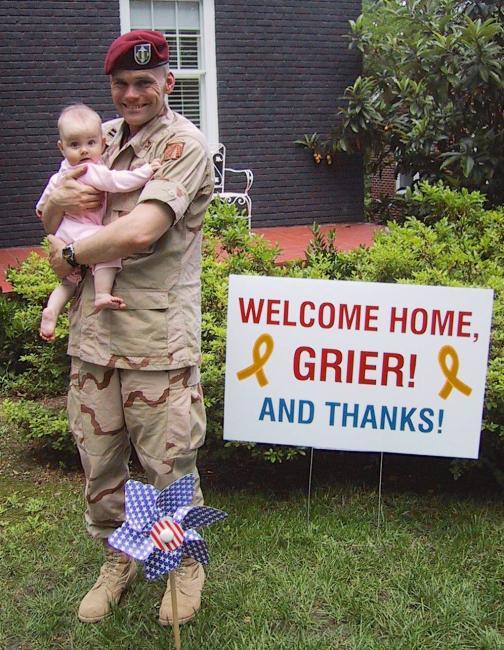 Grier Martin holding a baby in front of a Welcome Home sign
