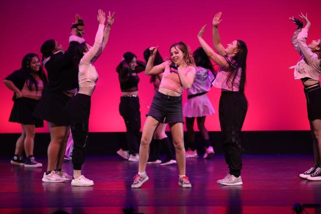 students dancing on stage with pink backdrop