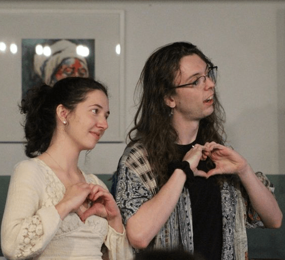 two students smiling and singing with hands formed in heart shape