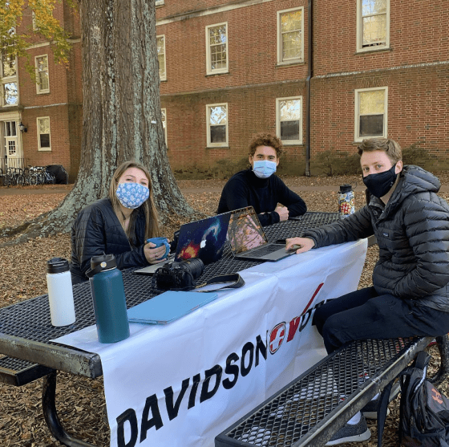 Students in masks outside with sign that says "Davidson Votes"