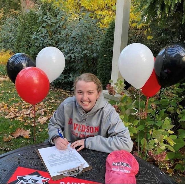 student signing paper with balloons and davidson gear