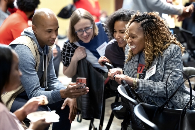 men and women gathered around a phone smiling and talking