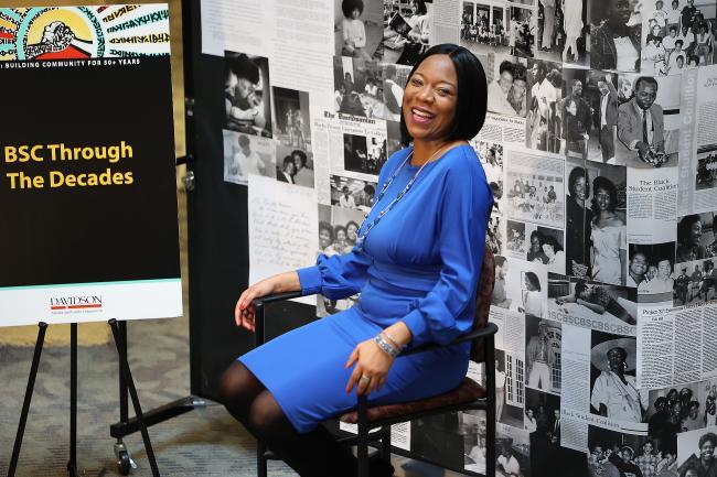 Black woman smiling in front of "BSC Through the Decades" exhibit