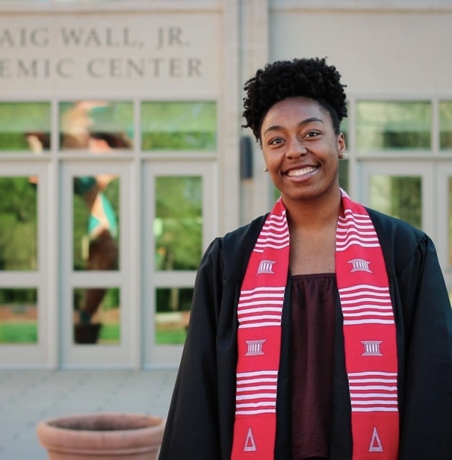 Woman wearing grad robes in front of Wall