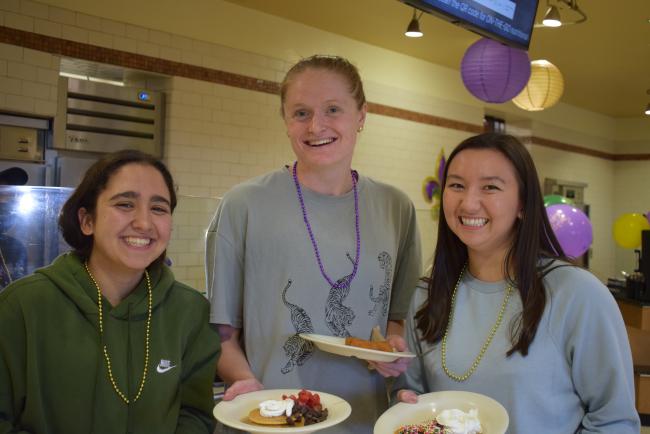Three students holding plates of food and smiling