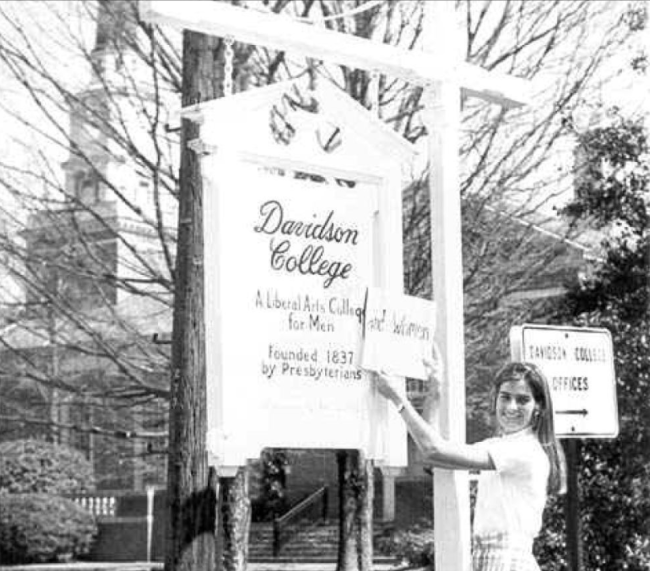 Woman holds a sign over another sign