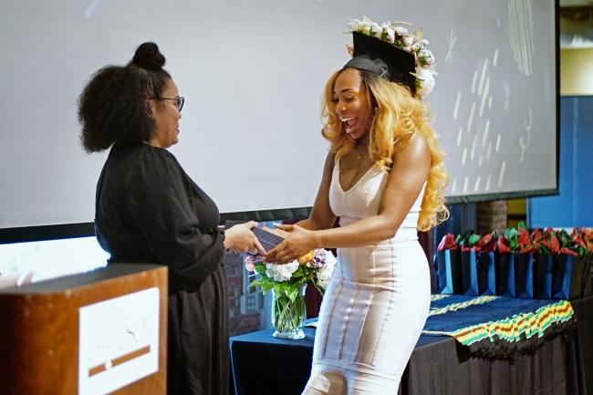 Two Black women embrace as one wears a decorated graduation cap