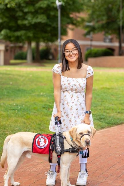 A young Asian woman smiles while holding the leash on her service dog