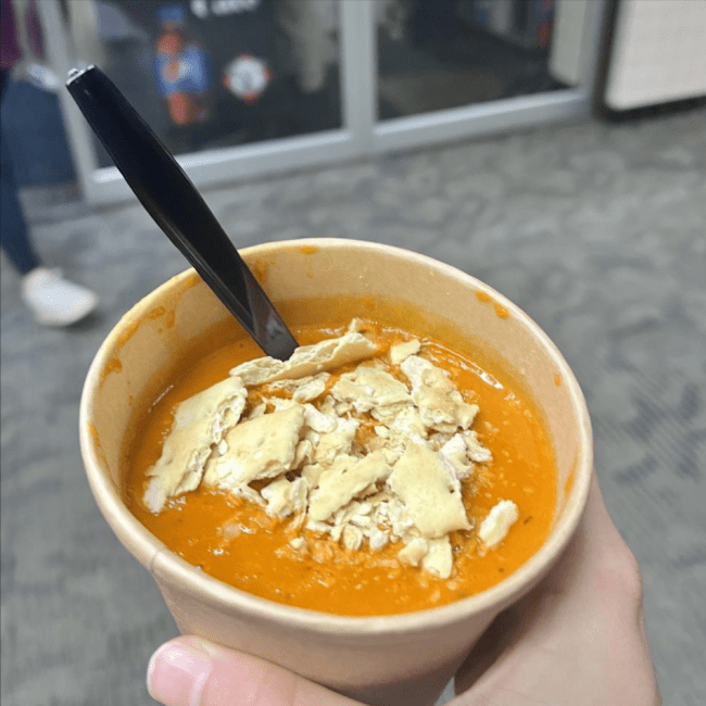 A hand holding a paper cup of soup
