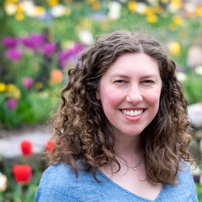 white woman with curly brown hair wearing a grey v-neck tshirt