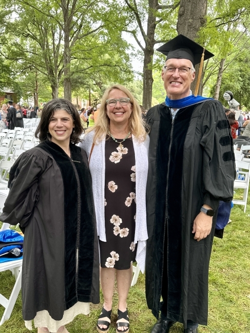 Two professors in commencement regalia with a woman in the middle