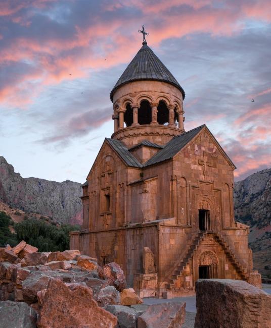 An old stone monastery in front of a pink and blue sunset sky