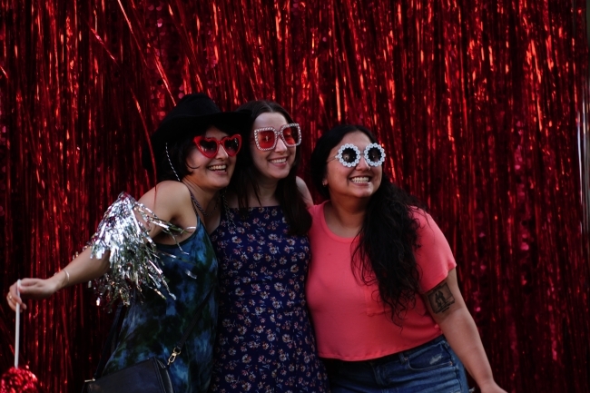 Young alumni smiling with glasses on and red back drop