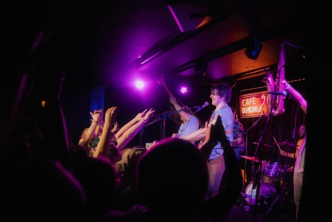 a group of young men play instruments on stage while hands in the crowd reach for them