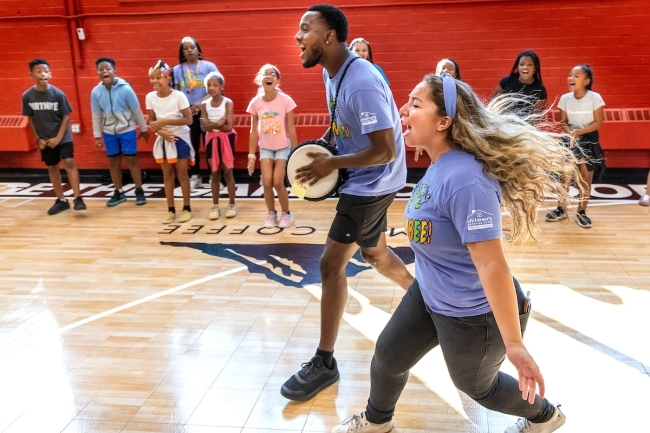 Students cheering while kids are in the background in a gym