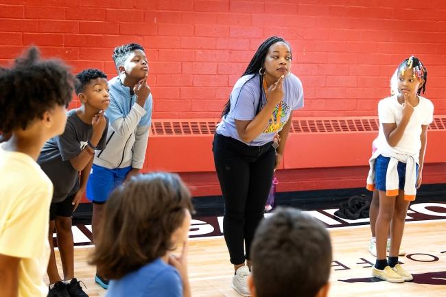 A young woman leads students in exercise in gym