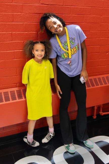 A student and a child smile together with a red brick wall behind them