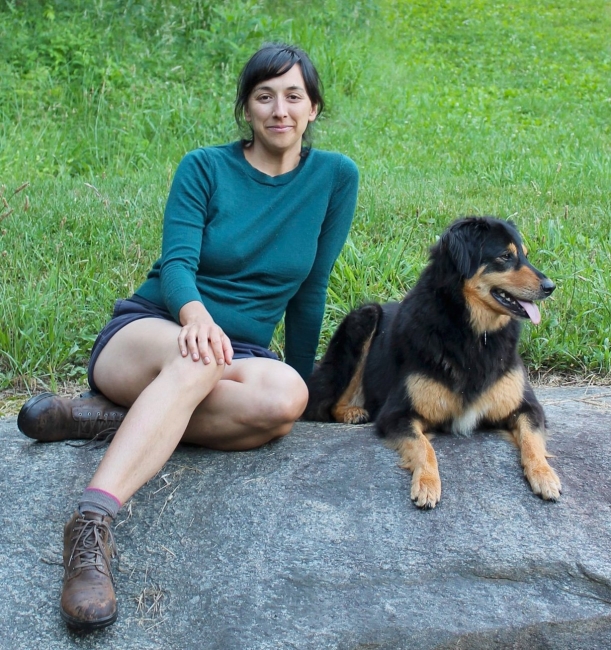 A woman wearing hiking boots sitting on a rock with her dog