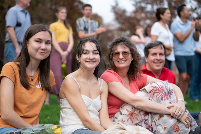 Two students and their families sitting on ground and smiling