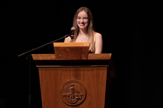 student speaks and smiles at podium on stage