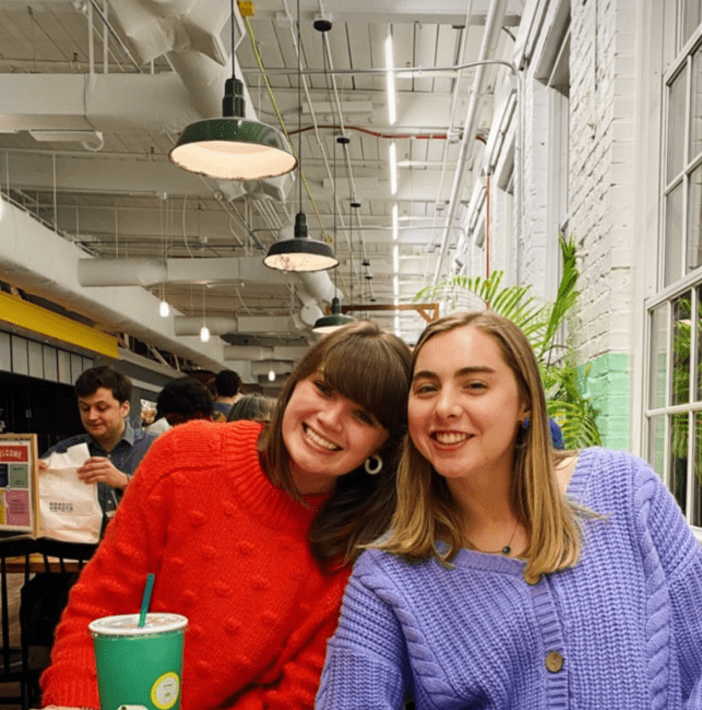 two young women smiling in sweaters in a food hall