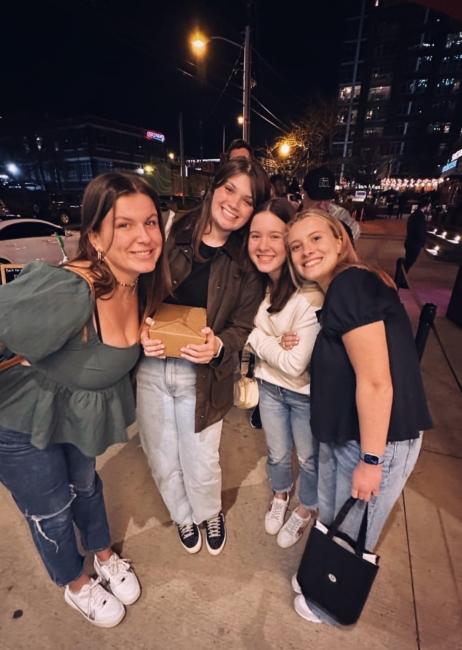 a group of four young women on city sidewalk at night smiling