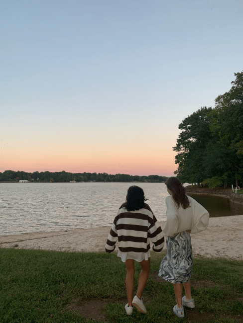 two students walk in front of a lake as the sun sets