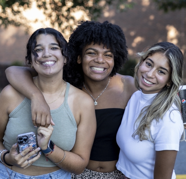 three students standing and smiling together