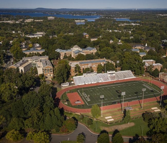 an aerial view of Davidson College campus with a football field in the foreground and a lake in the background
