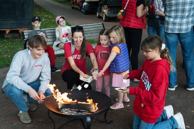 a group of people of all ages gathered around a fire roasting marshmallows