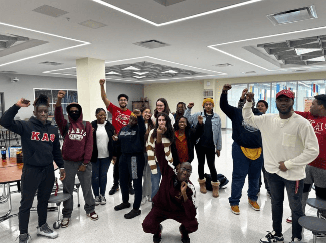 a group of students, college and high school, in a high school cafeteria smiling