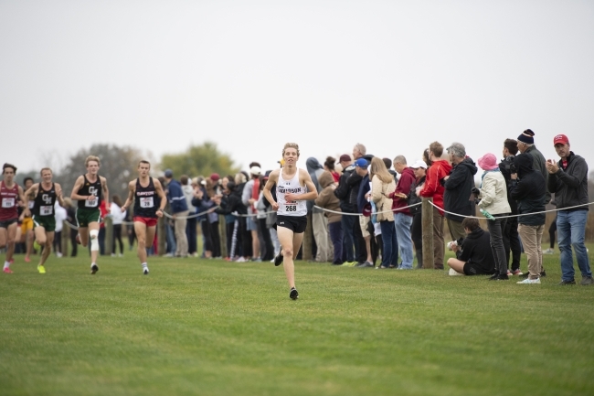 a young man runs a cross country race across a grassy field on a foggy day