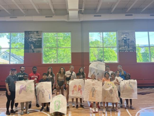 a group of college students with children holding posters in a gym