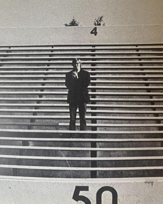 a black and white photograph of a young man standing in a stadium