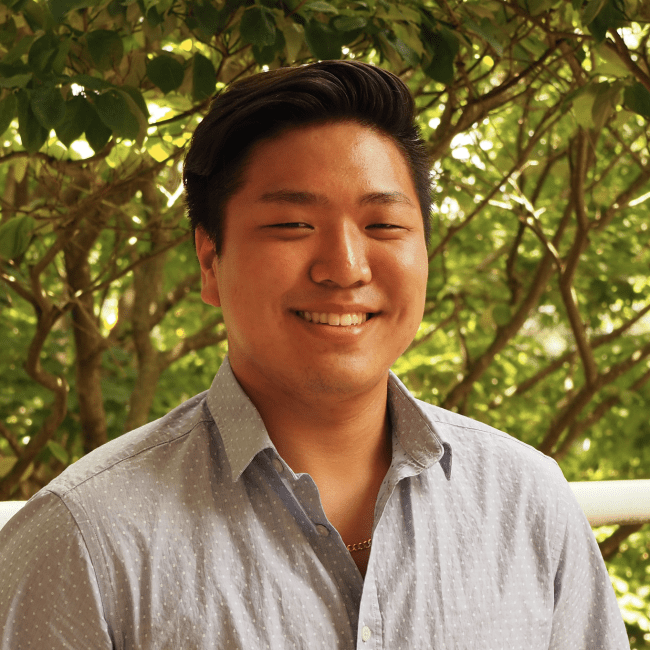 a young Asian man wearing a button-up and smiling